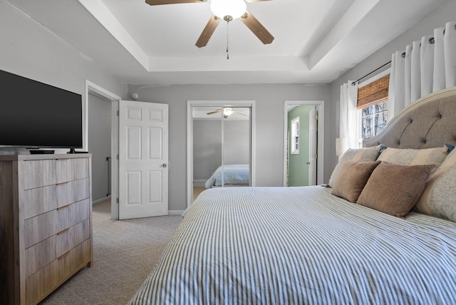 bedroom with a raised ceiling, light colored carpet, a closet, and baseboards