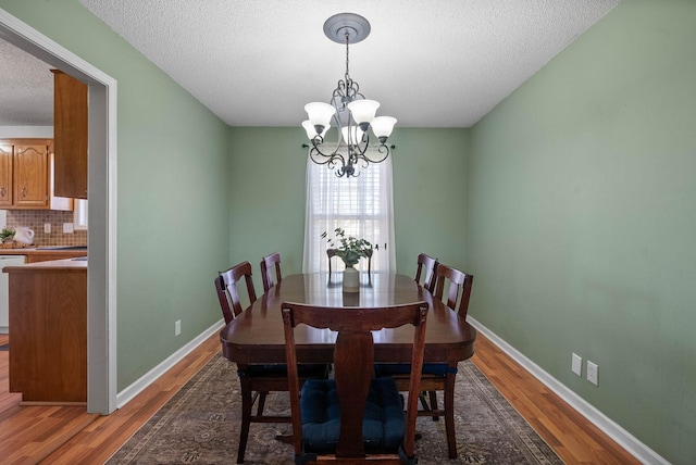 dining room featuring baseboards, light wood-style floors, a chandelier, and a textured ceiling