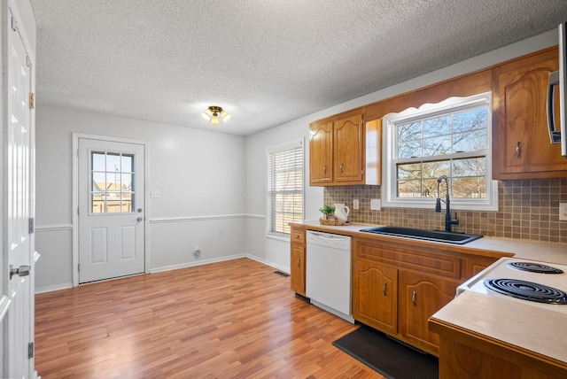 kitchen with brown cabinetry, light wood finished floors, white dishwasher, a sink, and light countertops