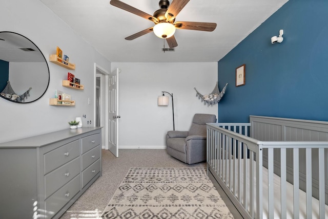 carpeted bedroom featuring a crib, visible vents, a ceiling fan, and baseboards