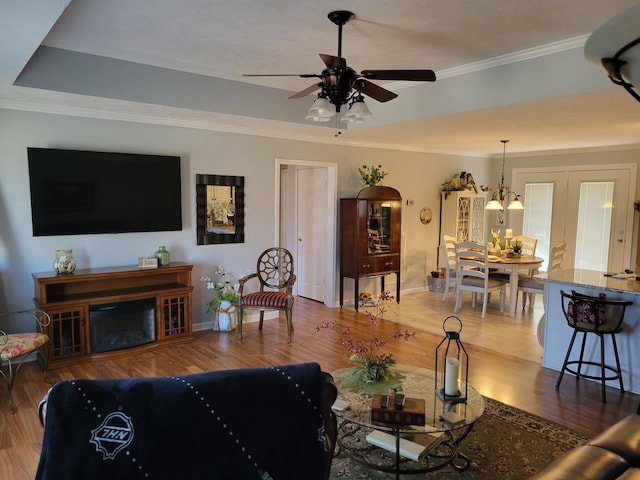 living room with ornamental molding, a ceiling fan, a glass covered fireplace, wood finished floors, and baseboards