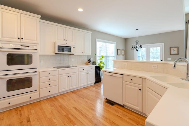 kitchen with white appliances, light wood finished floors, a sink, light countertops, and white cabinetry