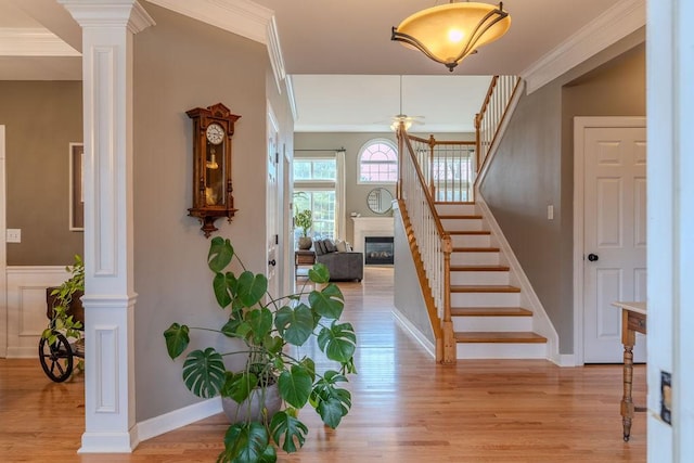 foyer with a glass covered fireplace, light wood-style flooring, stairway, and decorative columns