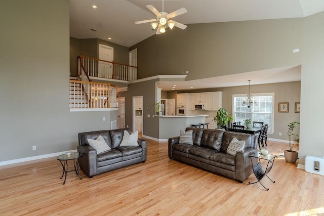 living area with baseboards, recessed lighting, ceiling fan with notable chandelier, light wood-style floors, and high vaulted ceiling