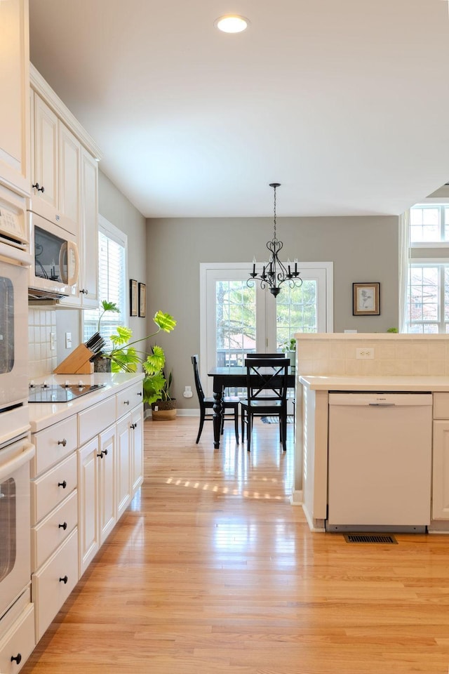 kitchen with backsplash, pendant lighting, light countertops, light wood-style floors, and white appliances