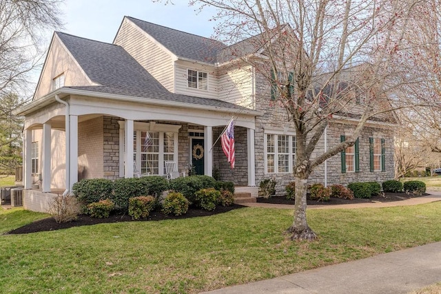 view of front of home with stone siding, roof with shingles, central AC, and a front yard