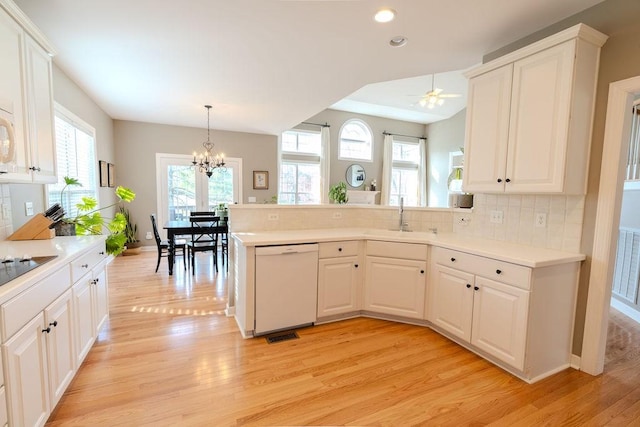 kitchen featuring light wood-style flooring, a sink, backsplash, white appliances, and a peninsula