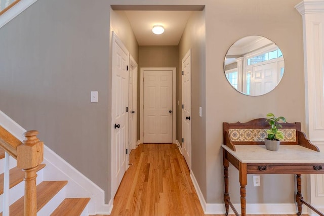 corridor featuring light wood finished floors, stairs, and baseboards