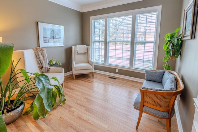 living area with visible vents, baseboards, wood finished floors, and crown molding