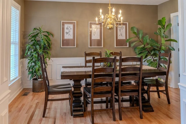 dining space featuring visible vents, wainscoting, a decorative wall, and light wood-style floors