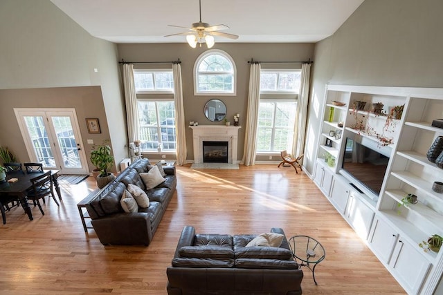 living area featuring light wood finished floors, a towering ceiling, ceiling fan, and a premium fireplace