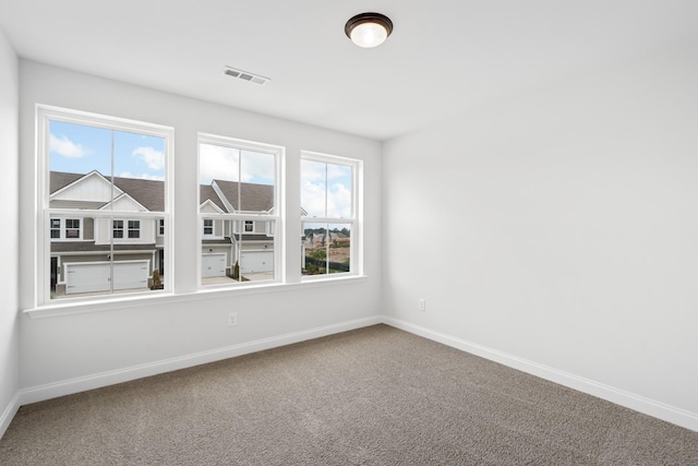 carpeted empty room featuring a wealth of natural light, visible vents, and baseboards