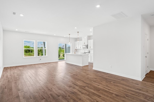 unfurnished living room with visible vents, a sink, wood finished floors, recessed lighting, and baseboards