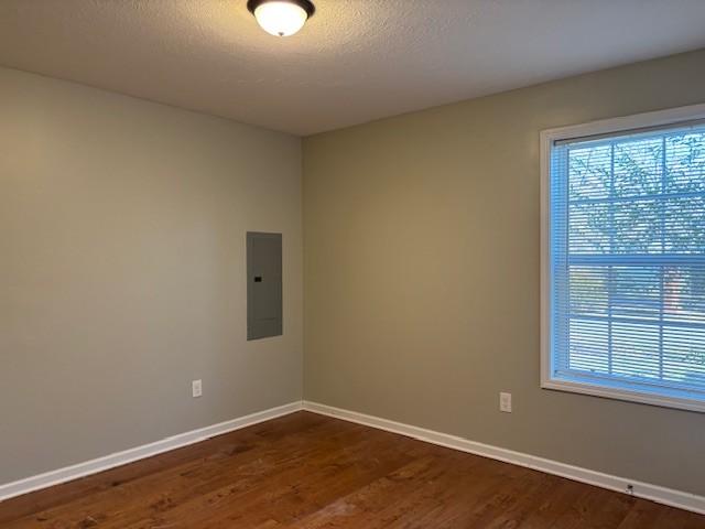 unfurnished room featuring electric panel, a textured ceiling, dark wood-type flooring, and baseboards