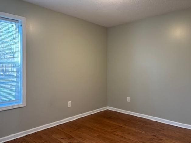 spare room featuring baseboards and dark wood finished floors