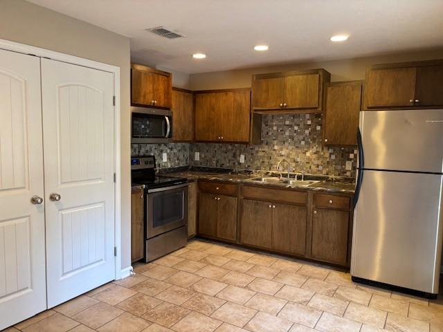 kitchen with dark countertops, visible vents, backsplash, stainless steel appliances, and a sink