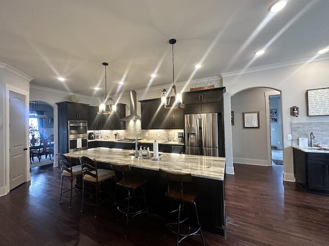 kitchen with arched walkways, stainless steel appliances, wall chimney range hood, and a sink