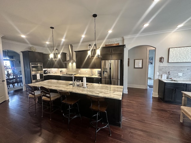 kitchen featuring a sink, stainless steel appliances, arched walkways, and wall chimney range hood