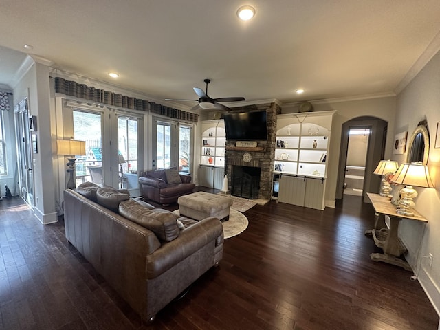 living room with arched walkways, ornamental molding, a fireplace, and dark wood-style flooring