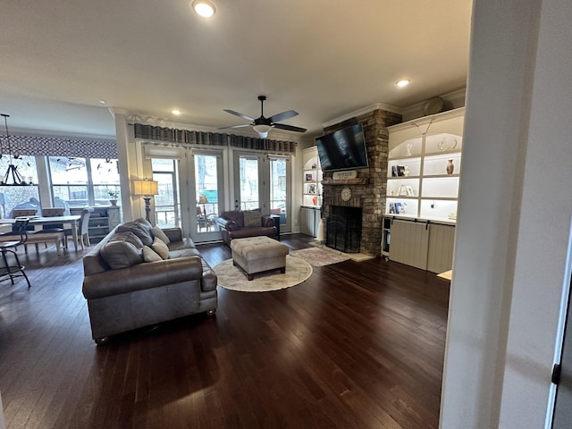 living room featuring dark wood finished floors, a stone fireplace, crown molding, and ceiling fan