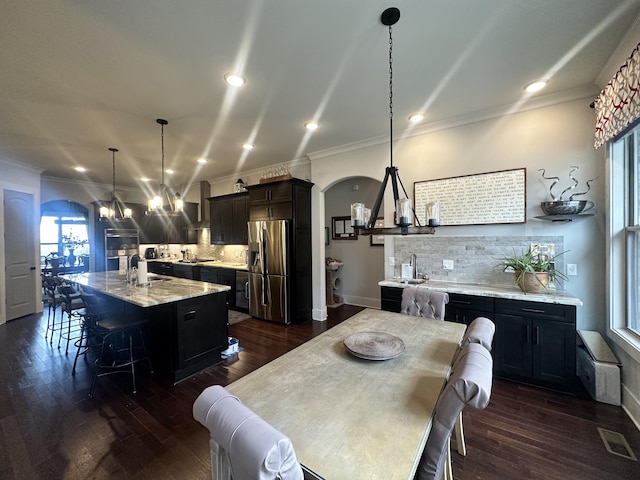 dining area featuring dark wood-type flooring, crown molding, arched walkways, and a chandelier