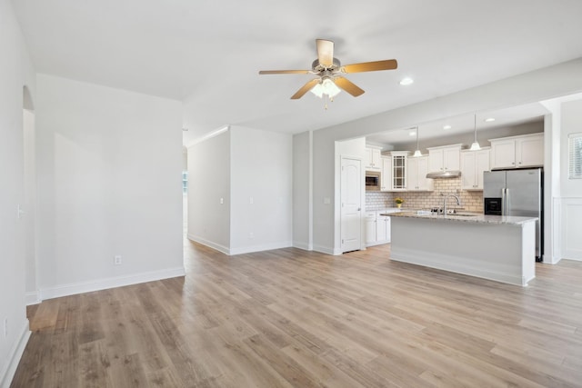 unfurnished living room featuring light wood finished floors, baseboards, recessed lighting, a ceiling fan, and a sink