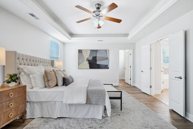 bedroom with a tray ceiling, multiple windows, wood finished floors, and visible vents