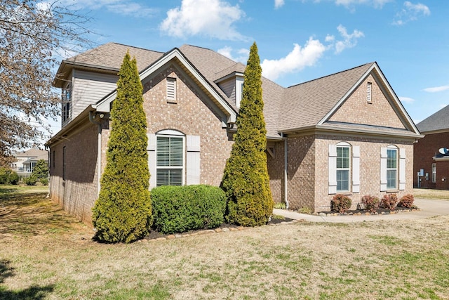 view of front of property featuring brick siding, a front yard, and a shingled roof