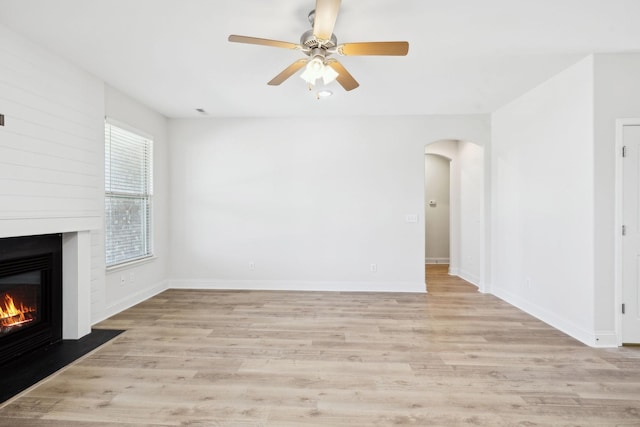 unfurnished living room featuring baseboards, a large fireplace, light wood-style floors, and arched walkways