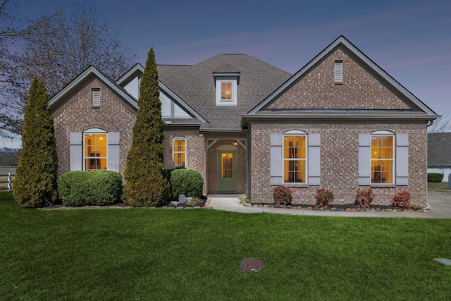 view of front of house with a front lawn, brick siding, and roof with shingles