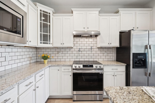 kitchen featuring stainless steel appliances, white cabinets, glass insert cabinets, under cabinet range hood, and backsplash