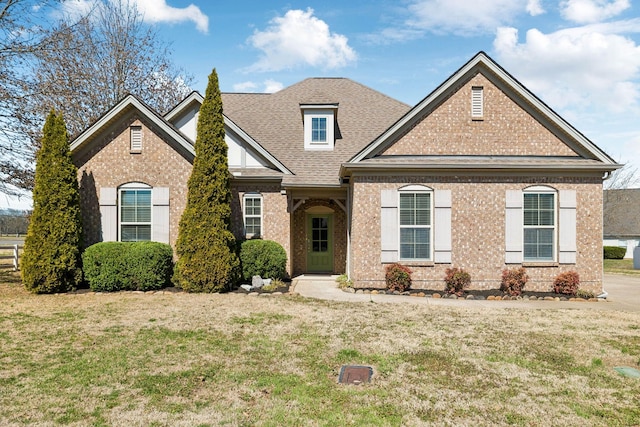 view of front of home featuring brick siding, a front yard, and roof with shingles