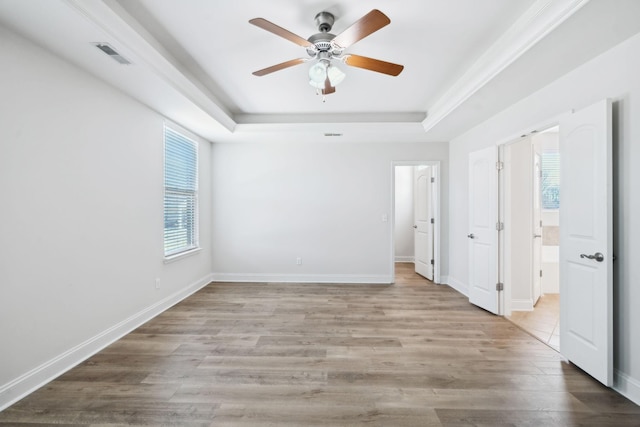 unfurnished bedroom featuring wood finished floors, visible vents, baseboards, ensuite bathroom, and a raised ceiling