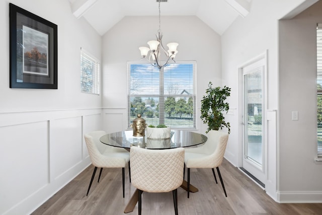 dining space featuring a chandelier, a wainscoted wall, vaulted ceiling, light wood-style flooring, and a decorative wall