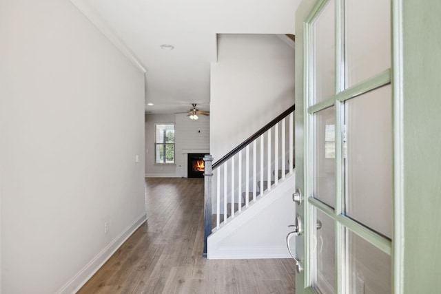 foyer entrance featuring a ceiling fan, wood finished floors, baseboards, recessed lighting, and a warm lit fireplace