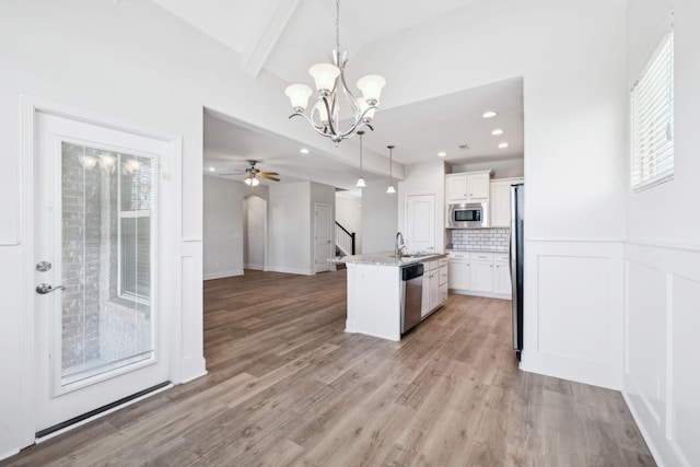 kitchen with stainless steel appliances, white cabinets, light wood-style floors, decorative light fixtures, and backsplash