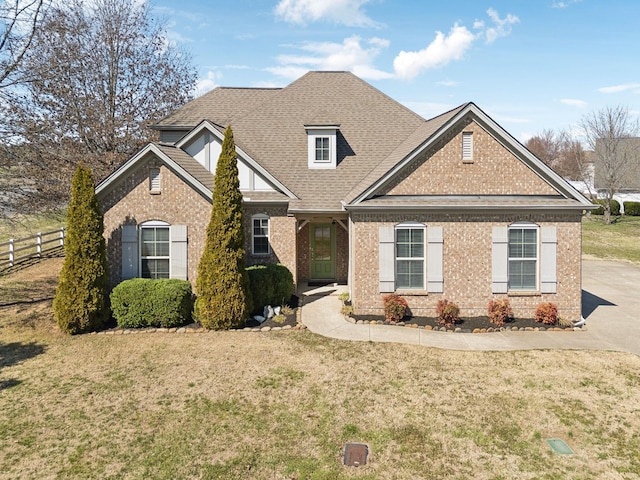 view of front of house featuring brick siding, a shingled roof, a front lawn, and fence