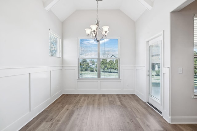 unfurnished dining area featuring a decorative wall, a notable chandelier, lofted ceiling, and light wood-style floors