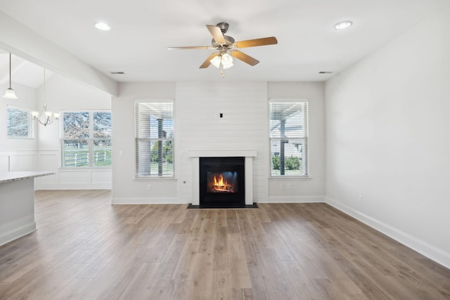 unfurnished living room with a fireplace, ceiling fan with notable chandelier, wood finished floors, and baseboards