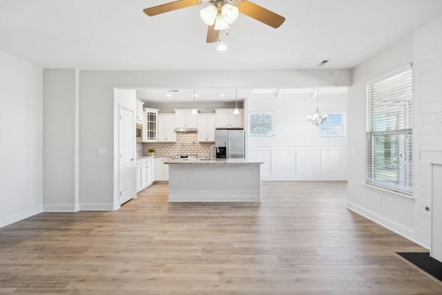 kitchen with a center island with sink, stainless steel refrigerator with ice dispenser, light wood-style floors, white cabinets, and decorative backsplash