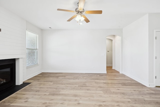 unfurnished living room featuring arched walkways, light wood-style flooring, a fireplace, and baseboards