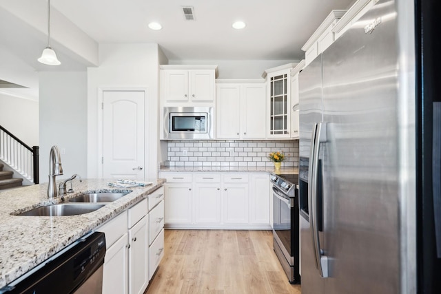 kitchen with visible vents, light wood-style flooring, a sink, decorative backsplash, and stainless steel appliances