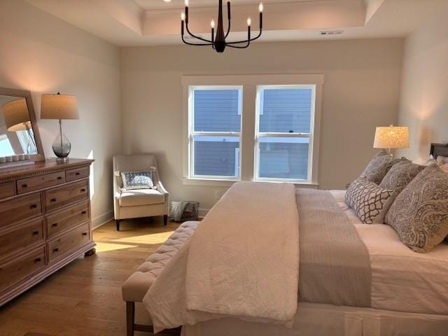 bedroom featuring an inviting chandelier, a raised ceiling, and light wood-style flooring