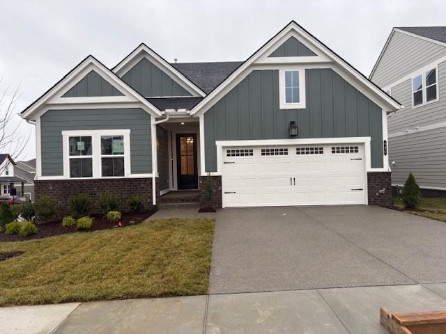 craftsman-style home featuring board and batten siding, concrete driveway, a front yard, a garage, and brick siding