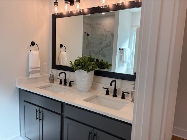 bathroom with double vanity, tiled shower, and a sink