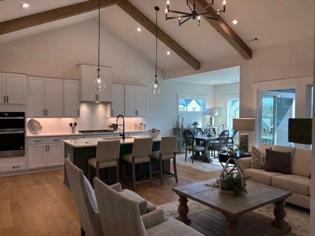 living room with visible vents, high vaulted ceiling, beamed ceiling, and light wood-style flooring