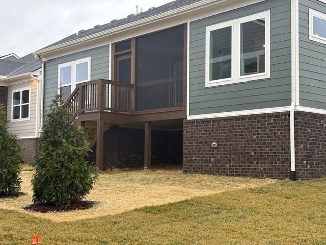 back of house featuring brick siding, a lawn, and a sunroom