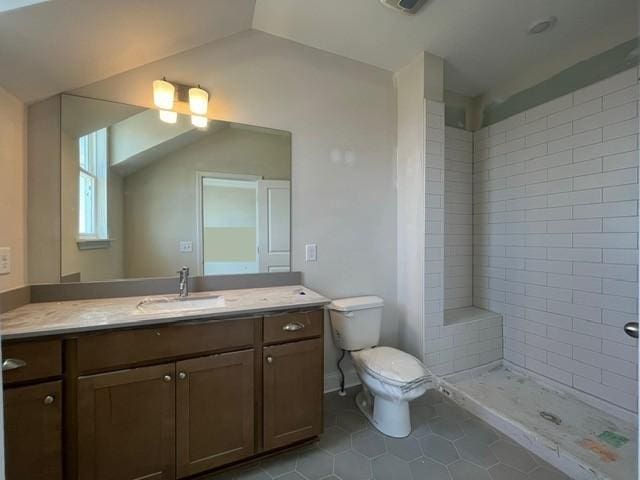 bathroom with vanity, lofted ceiling, a tile shower, tile patterned flooring, and toilet