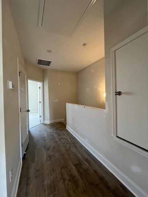 corridor with visible vents, attic access, dark wood-type flooring, and baseboards