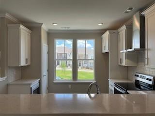 kitchen with light countertops, electric range, wall chimney exhaust hood, and crown molding